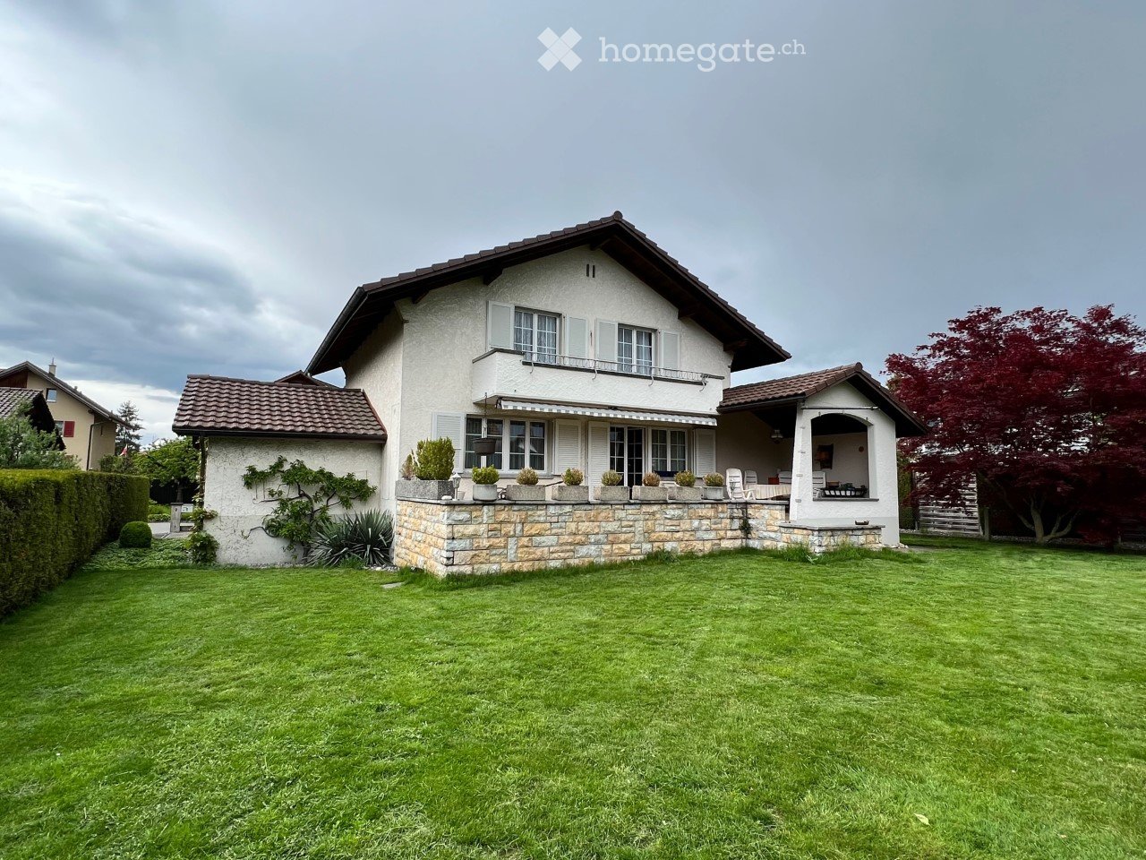 Two-story house with a stone base, white upper facade, multiple windows, and a well-maintained lawn.
