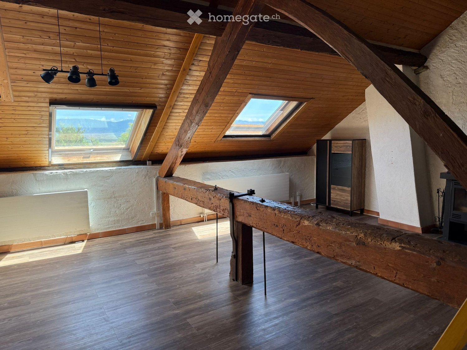 Loft-style room with wooden beams, skylights, a long wooden table, a cabinet, and a fireplace.