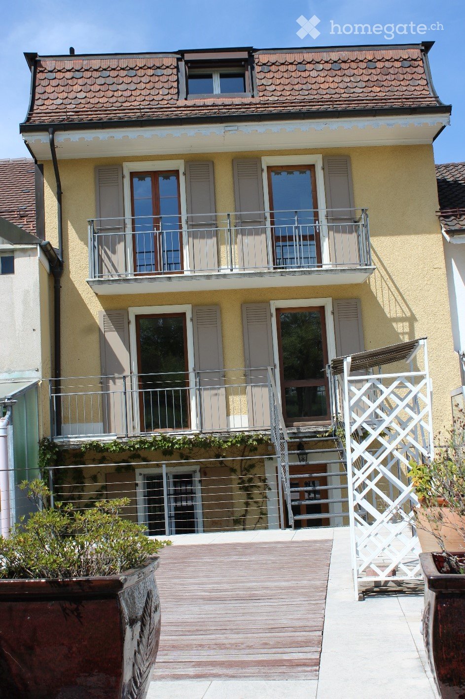 Two-story residential building with a balcony, wooden deck, and stairs leading to the entrance.