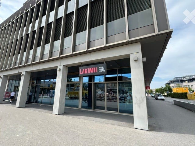 Modern commercial building entrance with large glass doors and a sign reading "LAKIMI III" above the entrance.