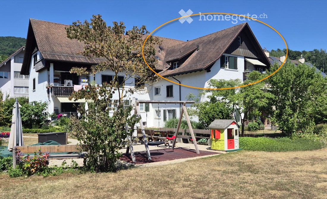 A two-story house with a brown roof and white walls, surrounded by a well-maintained garden with a swing set, a small playhouse, and a patio area.