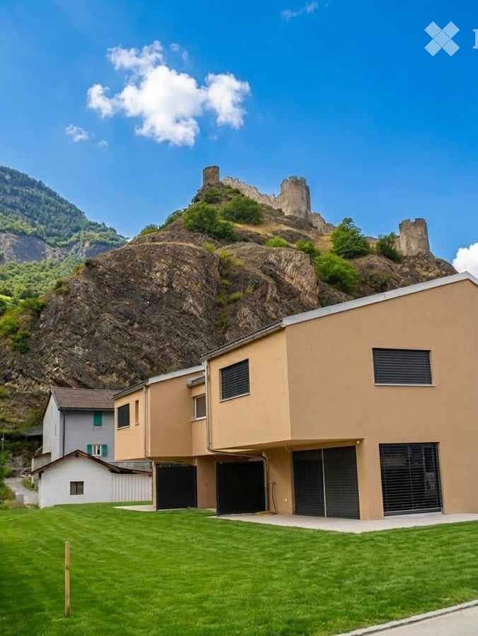 Modern two-story building with beige facade, large garage doors, and a well-maintained lawn, situated in front of a rocky hill with a castle-like structure on top.