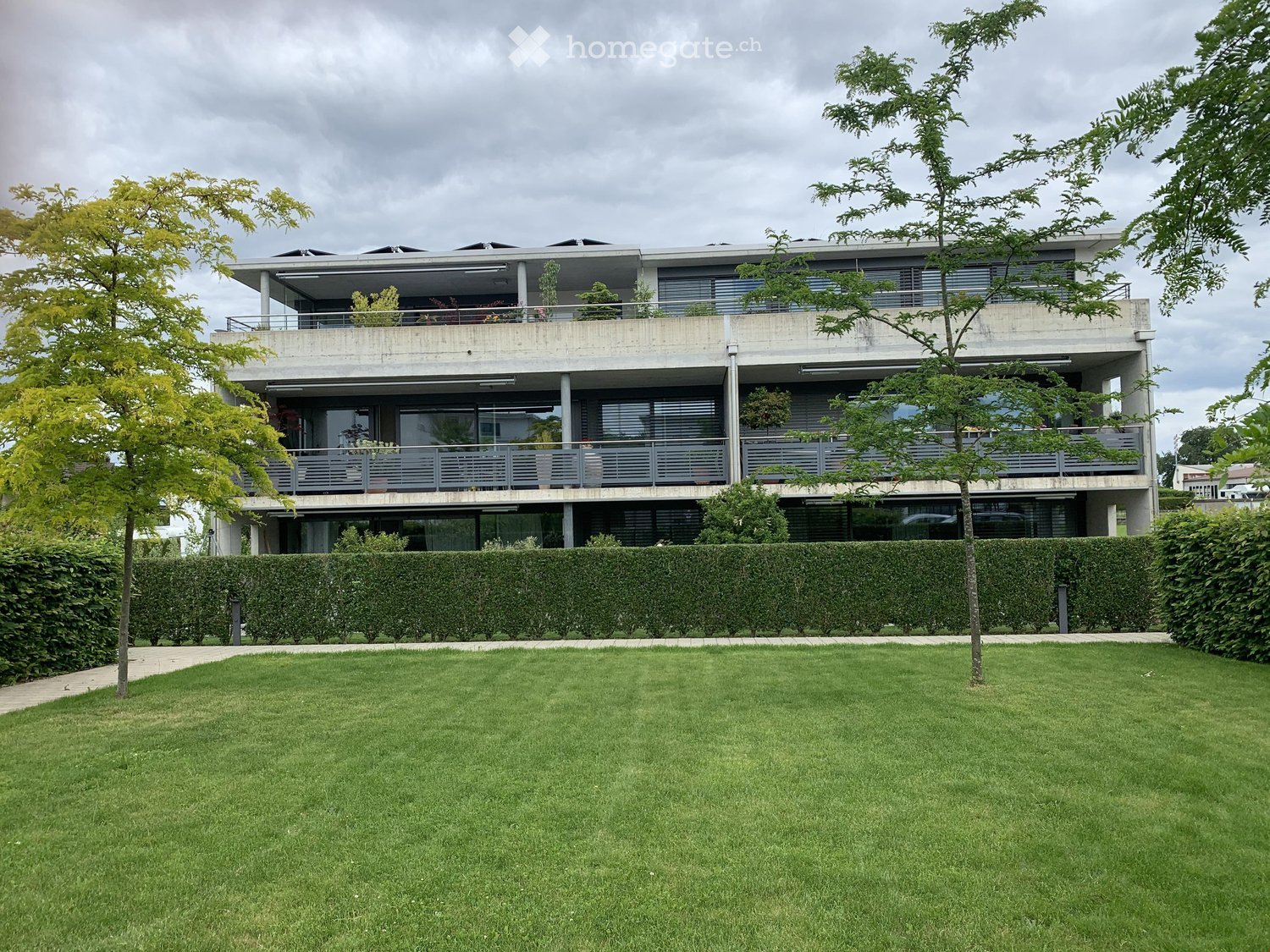 Modern two-story house with large windows, balconies, and a well-maintained lawn in front.
