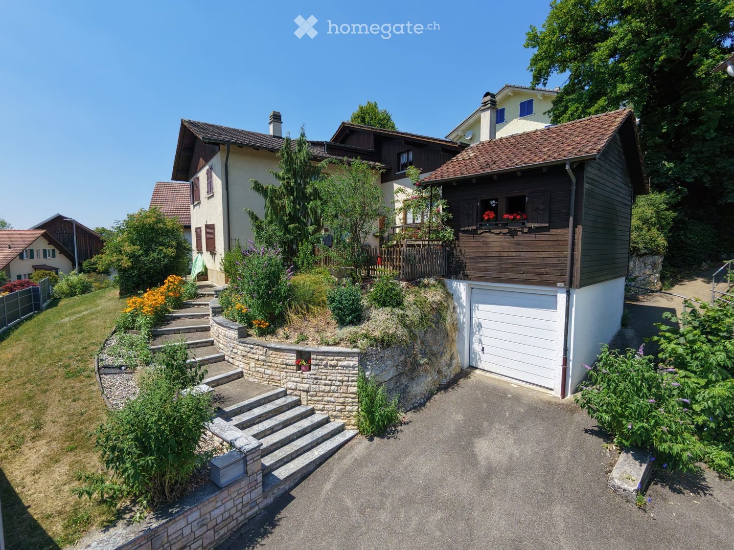 A two-story house with a brown tiled roof, white garage, and a landscaped garden with steps leading up to the house.
