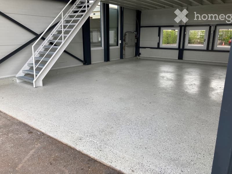 Empty garage with concrete floor, white metal staircase leading up, large windows, and industrial-style doors.