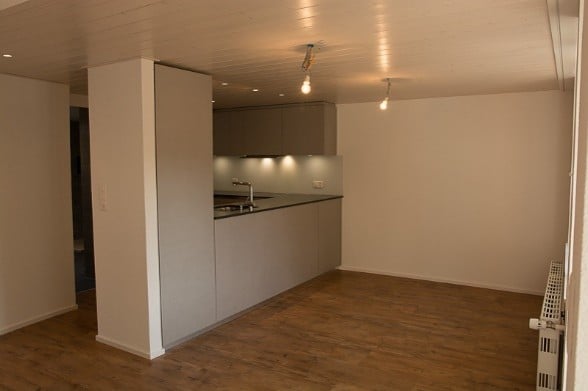 Modern, minimalist kitchen area with sleek cabinetry, a sink, and built-in lighting. The space is clean and contemporary, featuring light wood flooring and white walls.