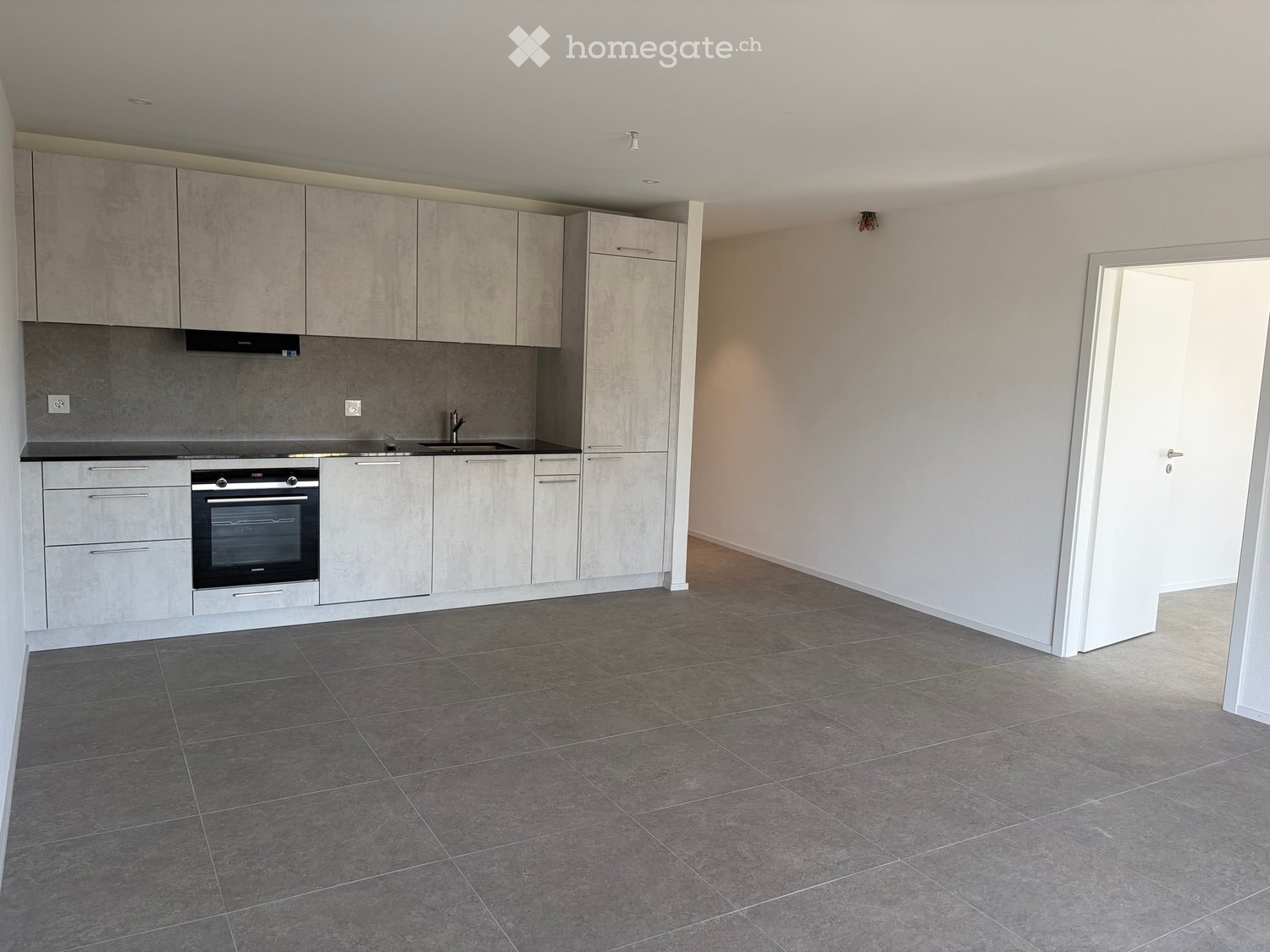Modern kitchen with grey tiled floor, grey cabinets, and stainless steel appliances including an oven and sink.