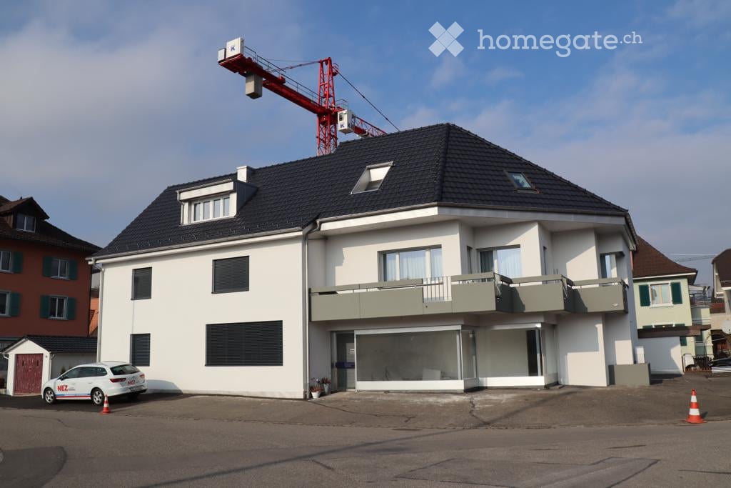 Two-story modern house with white exterior, dark roof, multiple windows, and a balcony on the upper floor.
