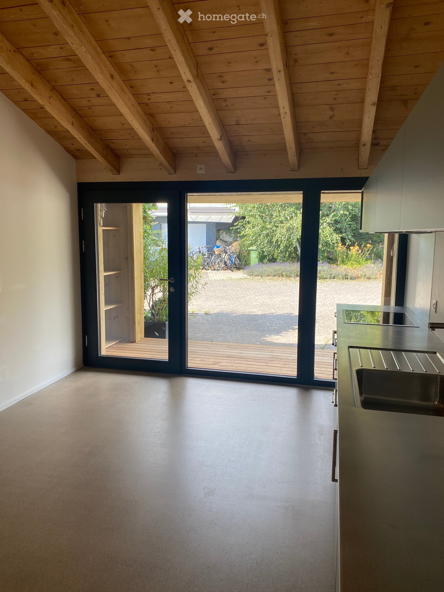 Modern kitchen with a sleek stainless steel sink, minimalist countertop, and large sliding glass doors leading to a wooden deck and garden area.