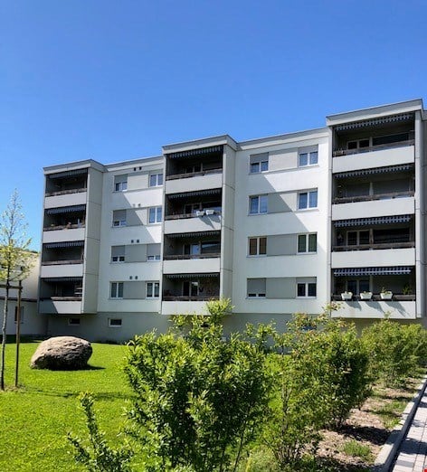 5 story apartment building, white, multiple balconies, garden in front, large rock