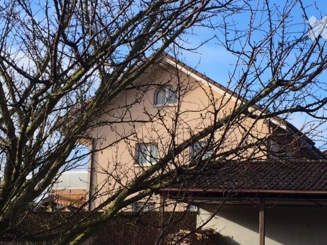 A two-story house with beige walls and multiple windows, partially obscured by leafless trees.