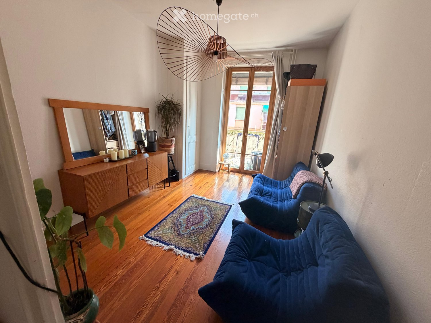 A cozy living room with wooden flooring, a large mirror, a blue sofa, a coffee table, and a decorative rug.
