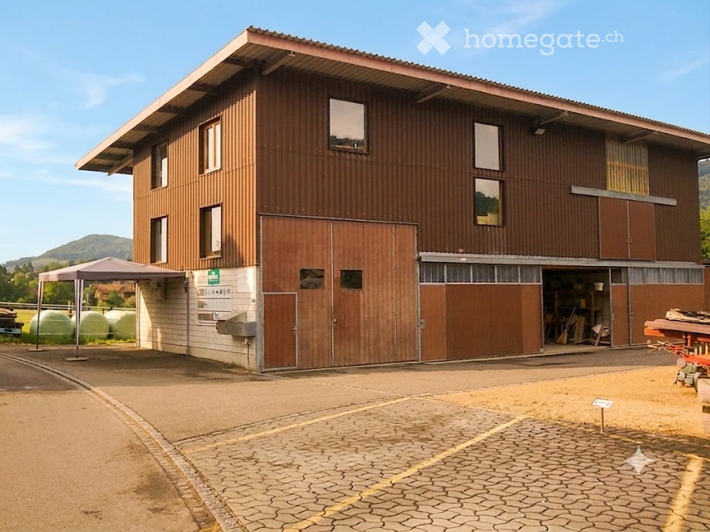 Two-story wooden building with large garage doors, multiple windows, and a covered outdoor area.