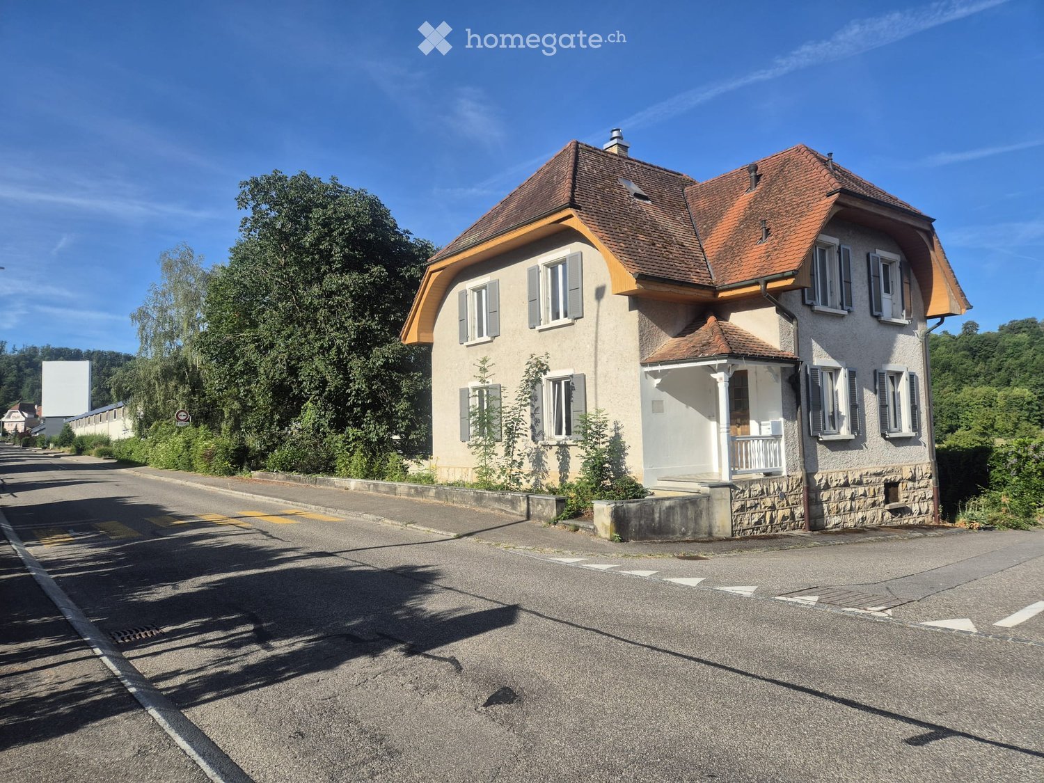 Two-story house with a red-tiled roof, multiple windows, and a small balcony on the right side.