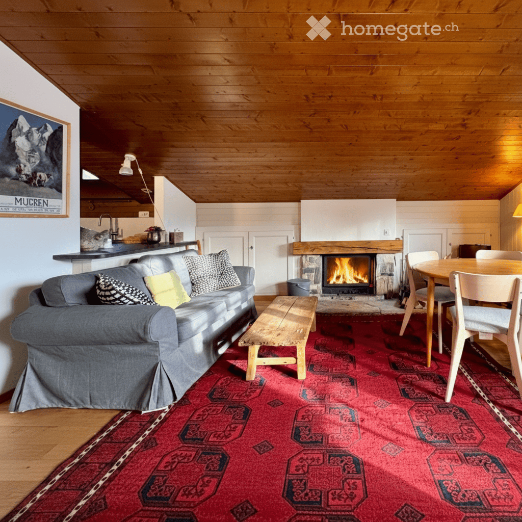 Cozy living room with wooden beams, a fireplace, a grey sofa, a wooden coffee table, and a dining area with a table and chairs.