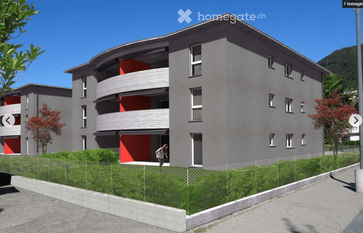 Modern multi-story residential building with grey facade, red accents, balconies, and surrounding greenery.