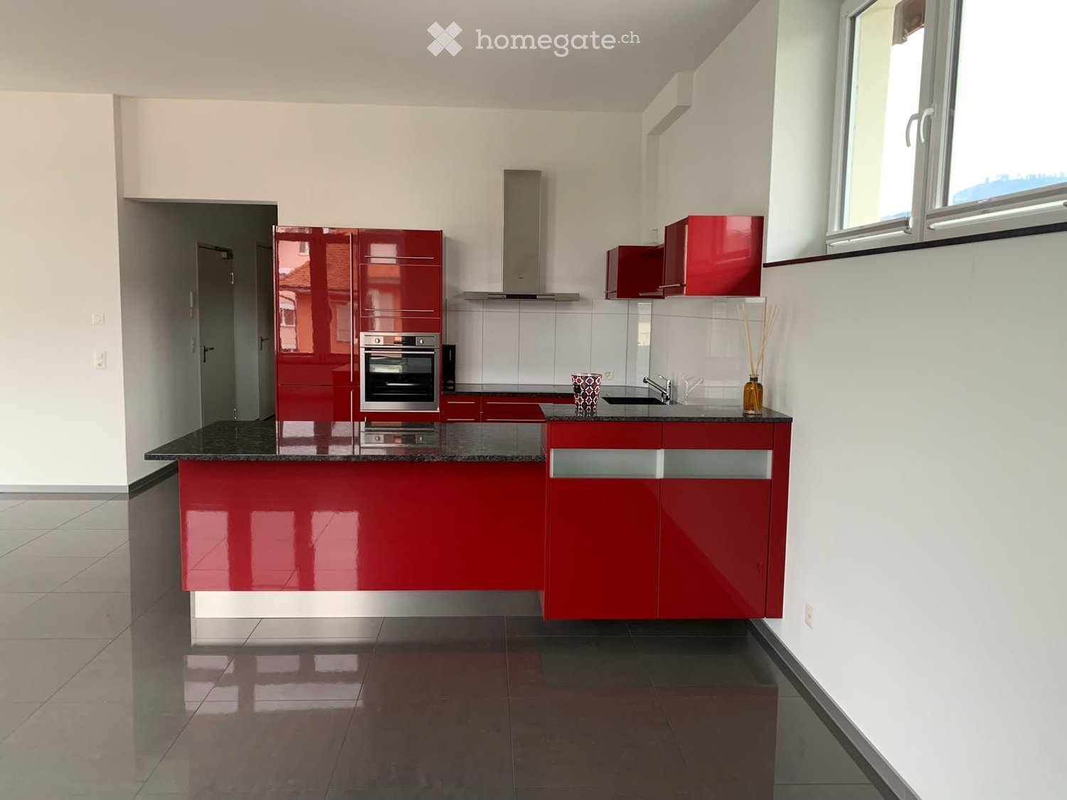 Modern kitchen with red cabinets, stainless steel oven, granite countertop, and large windows.