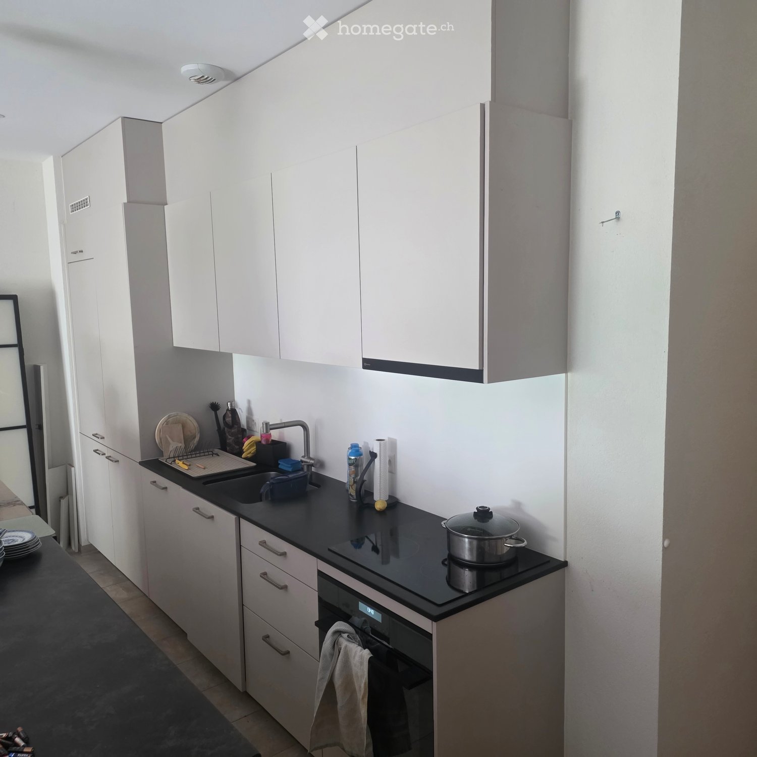 Modern kitchen with white cabinets, black countertop, sink, oven, and various kitchen items including a pot on the stove and a towel hanging from the oven handle.