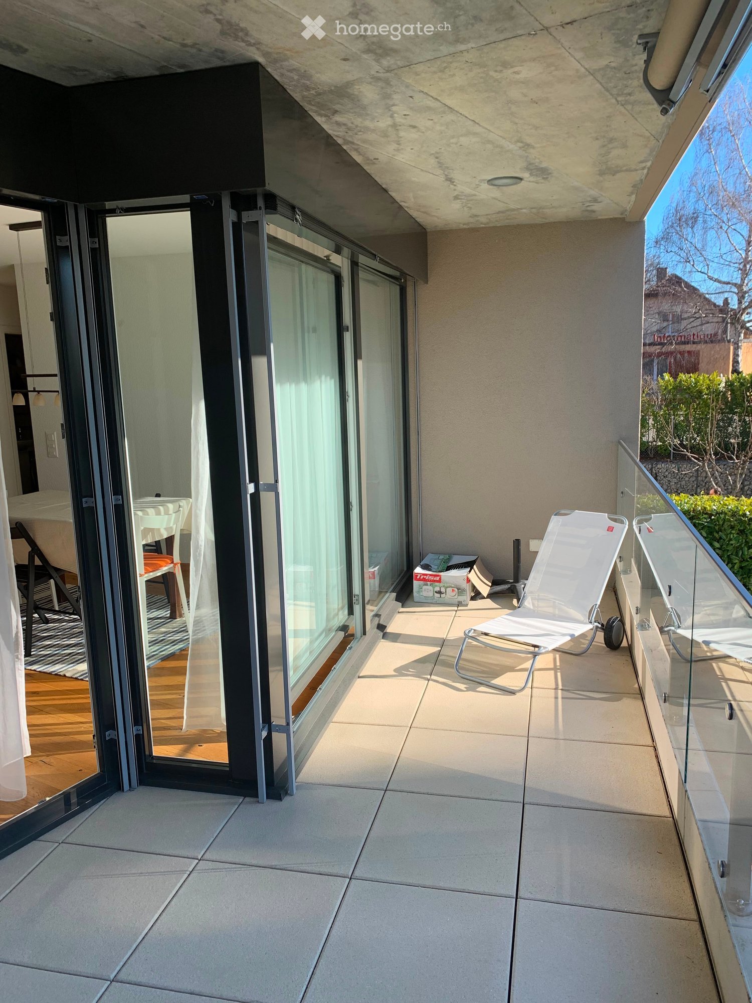 Balcony with tiled floor, glass railing, and a white lounge chair.