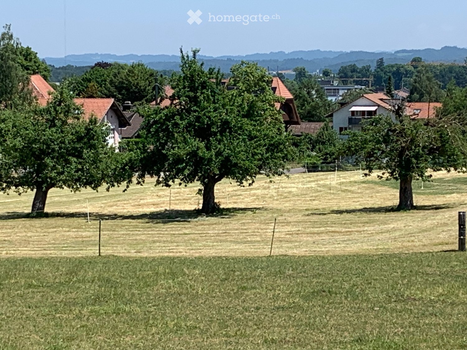 Rural landscape with scattered houses, trees, and open fields under a clear sky.