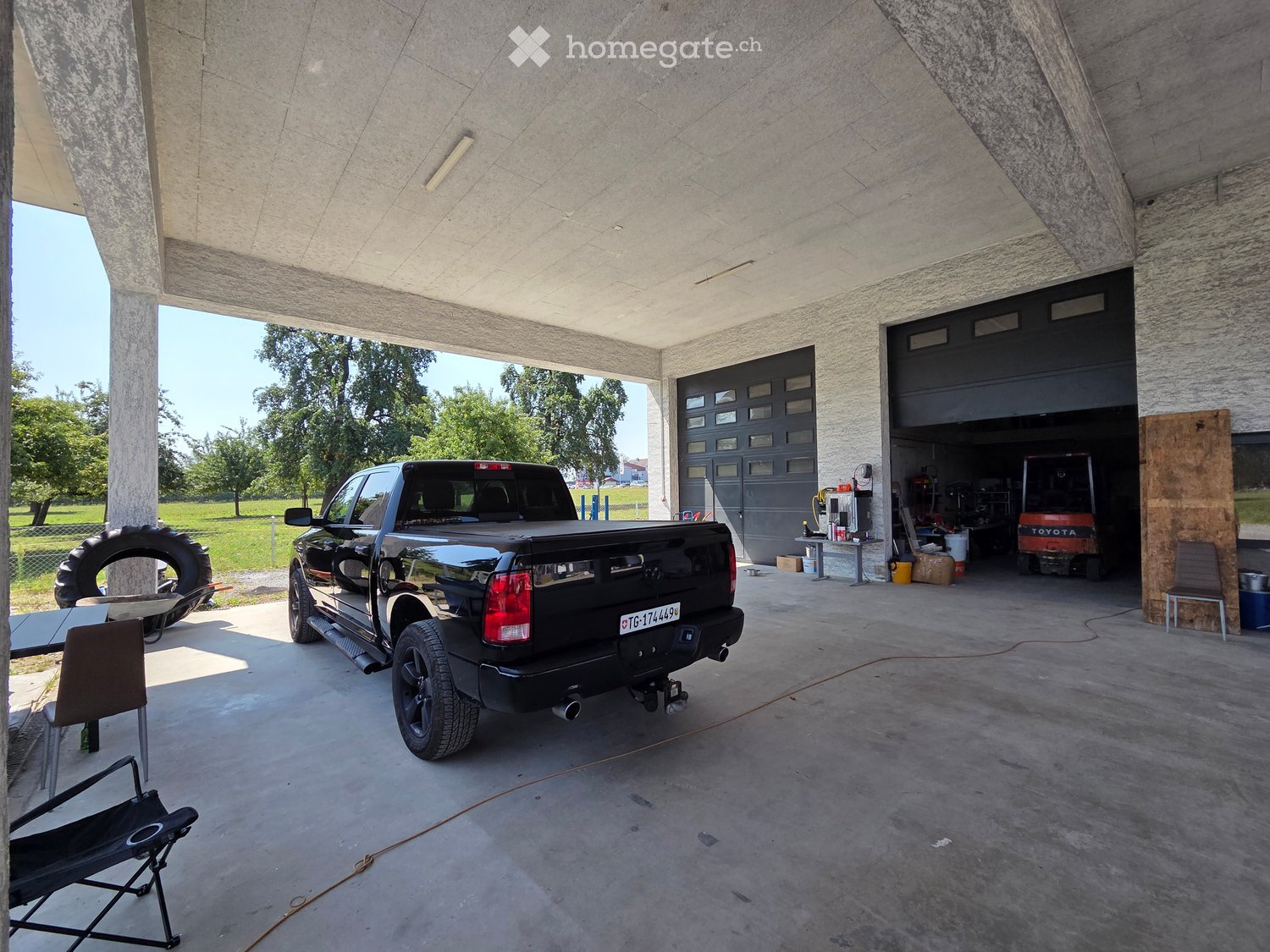 {"type": "Garage", "objects": [], "visible_features": ["Garage"], "description": "Modern garage with concrete walls and ceiling, featuring a black pickup truck, a tire, and a small folding chair."}