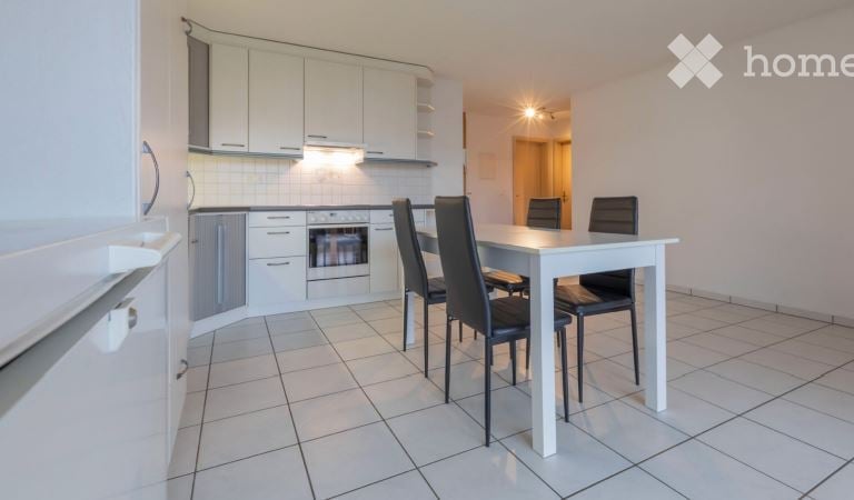 Bright, modern kitchen and dining area with white cabinets, a built-in oven, a refrigerator, and a white dining table with four black chairs.