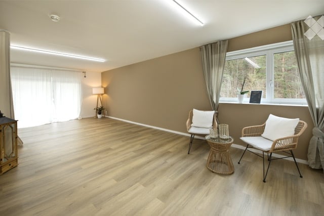 Empty room with wooden flooring, large windows, and neutral-colored walls. No furniture or equipment present.
