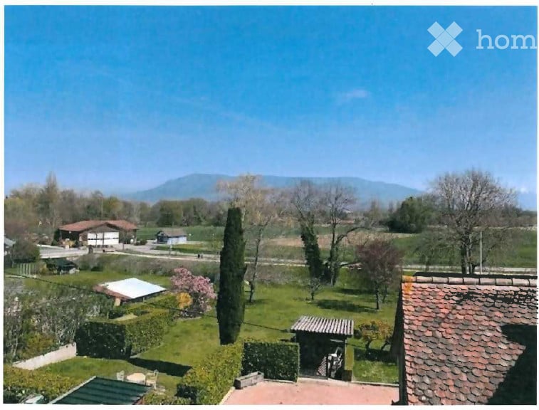 A peaceful garden with a view of the countryside and distant mountains, featuring a tall cypress tree, neatly trimmed hedges, and scattered trees.