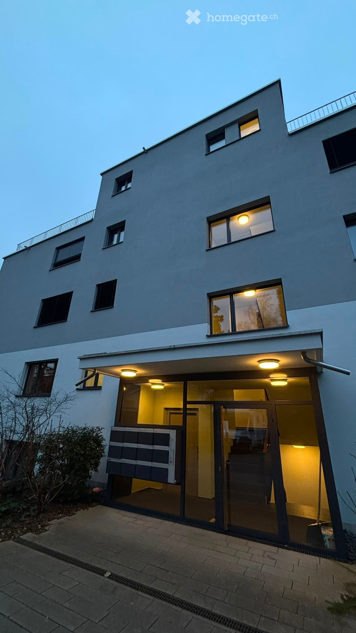 Modern two-story house with large windows, illuminated interior, and a raised ground floor entrance.