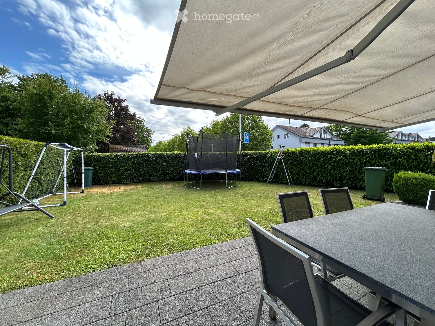 Backyard with a trampoline, swing set, patio furniture, and covered seating area.
