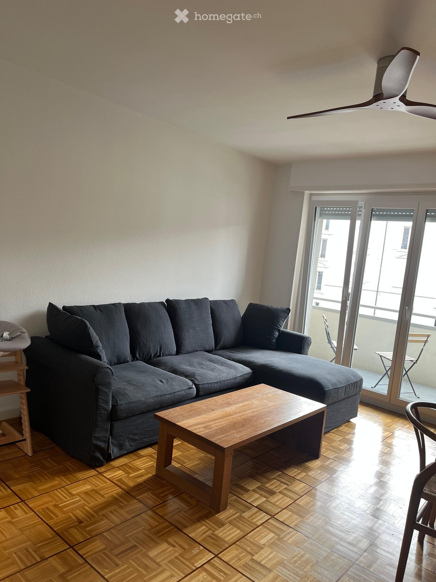 Modern living room with grey sectional sofa, wooden coffee table, and hardwood flooring, leading to a balcony.