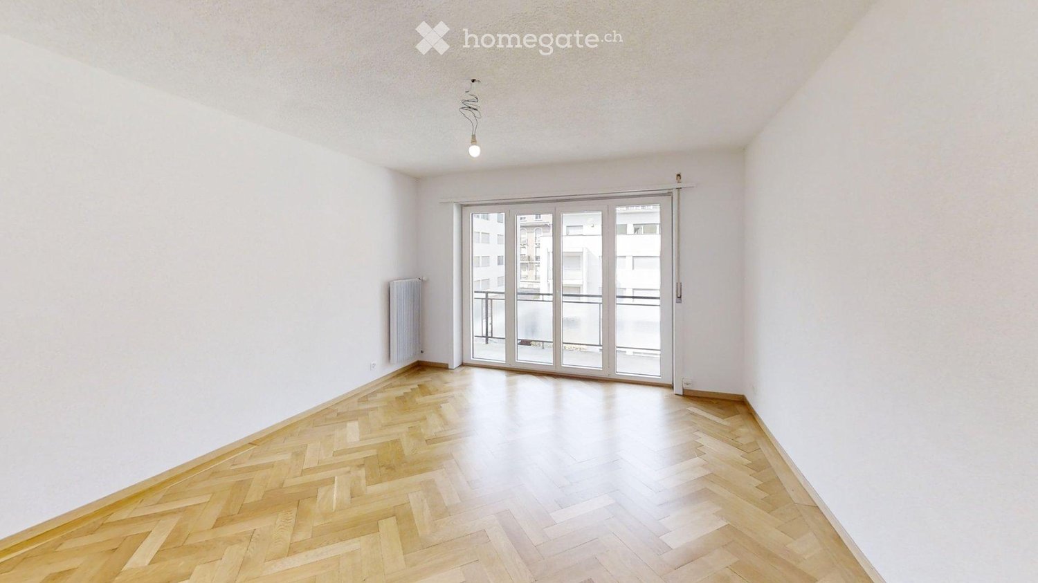 Empty room with wooden herringbone flooring, white walls, and large sliding glass doors leading to a balcony.