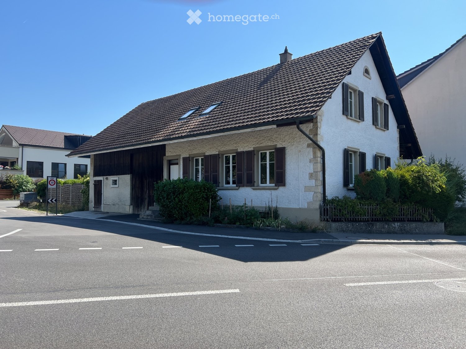 Two-story house with a tiled roof, white exterior, multiple windows with shutters, and a small garage.