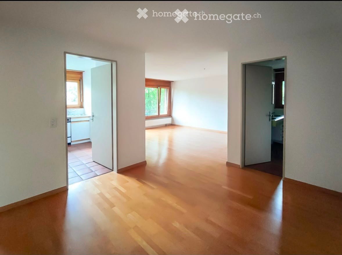Empty room with wooden flooring and white walls, featuring three open doorways leading to other rooms.