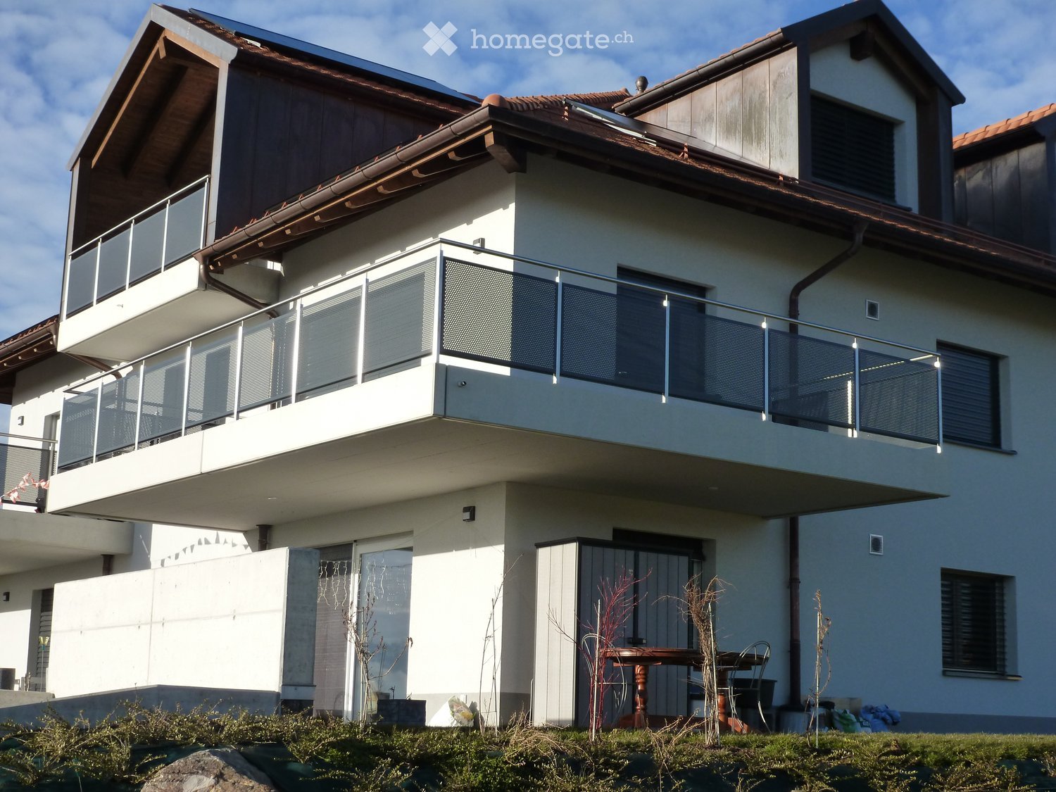 Two-story house with a balcony, modern design, and a small outdoor seating area with a table and chairs.
