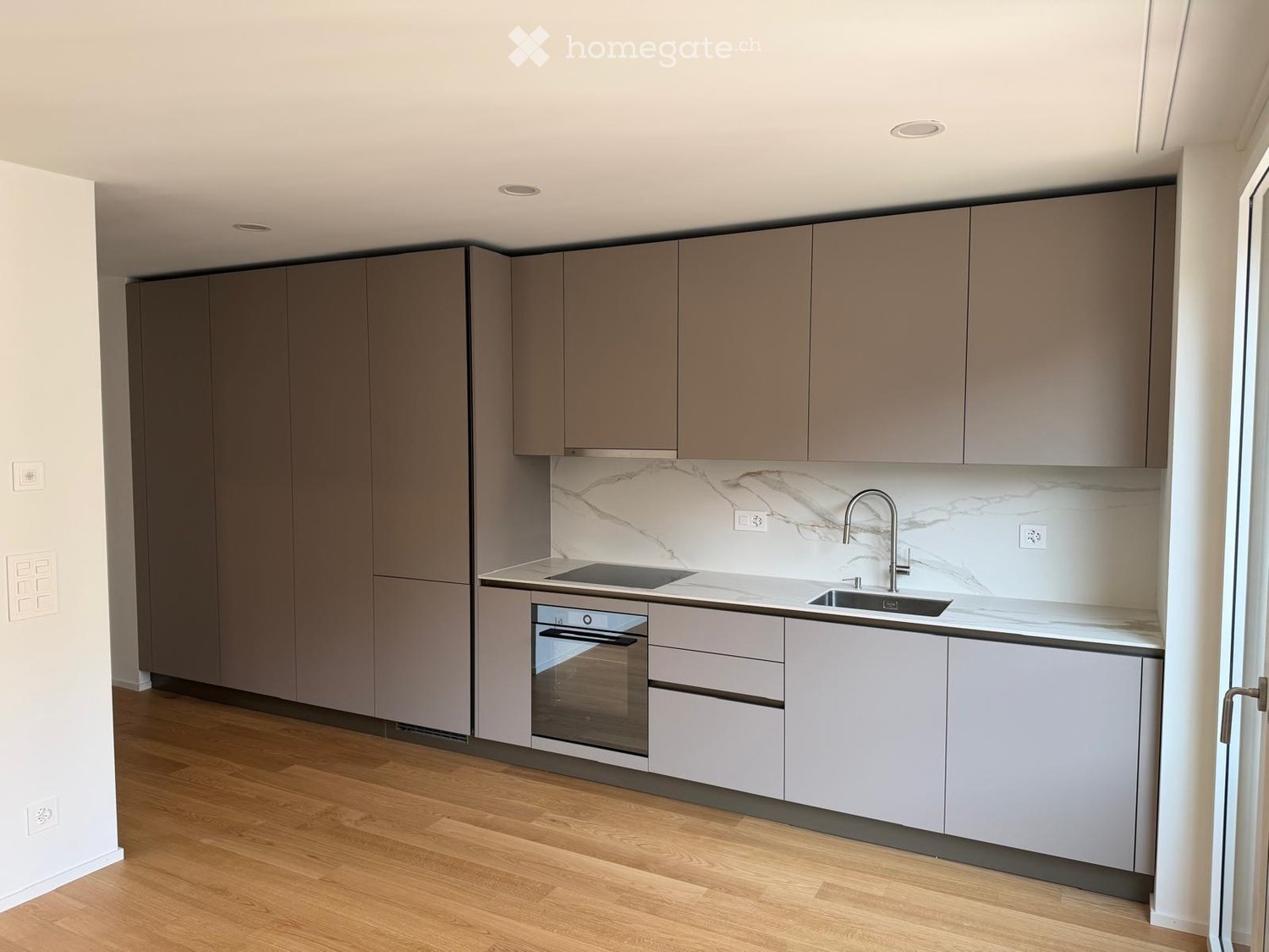 Modern kitchen with grey cabinets, marble backsplash, and wooden flooring.