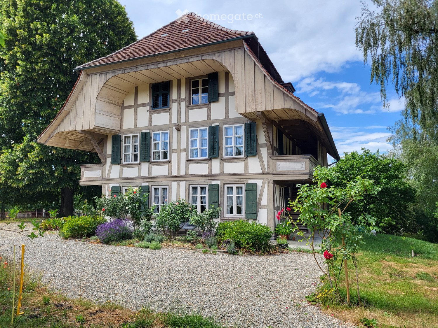 Two-story traditional house with wooden facade, green shutters, and a well-maintained garden.