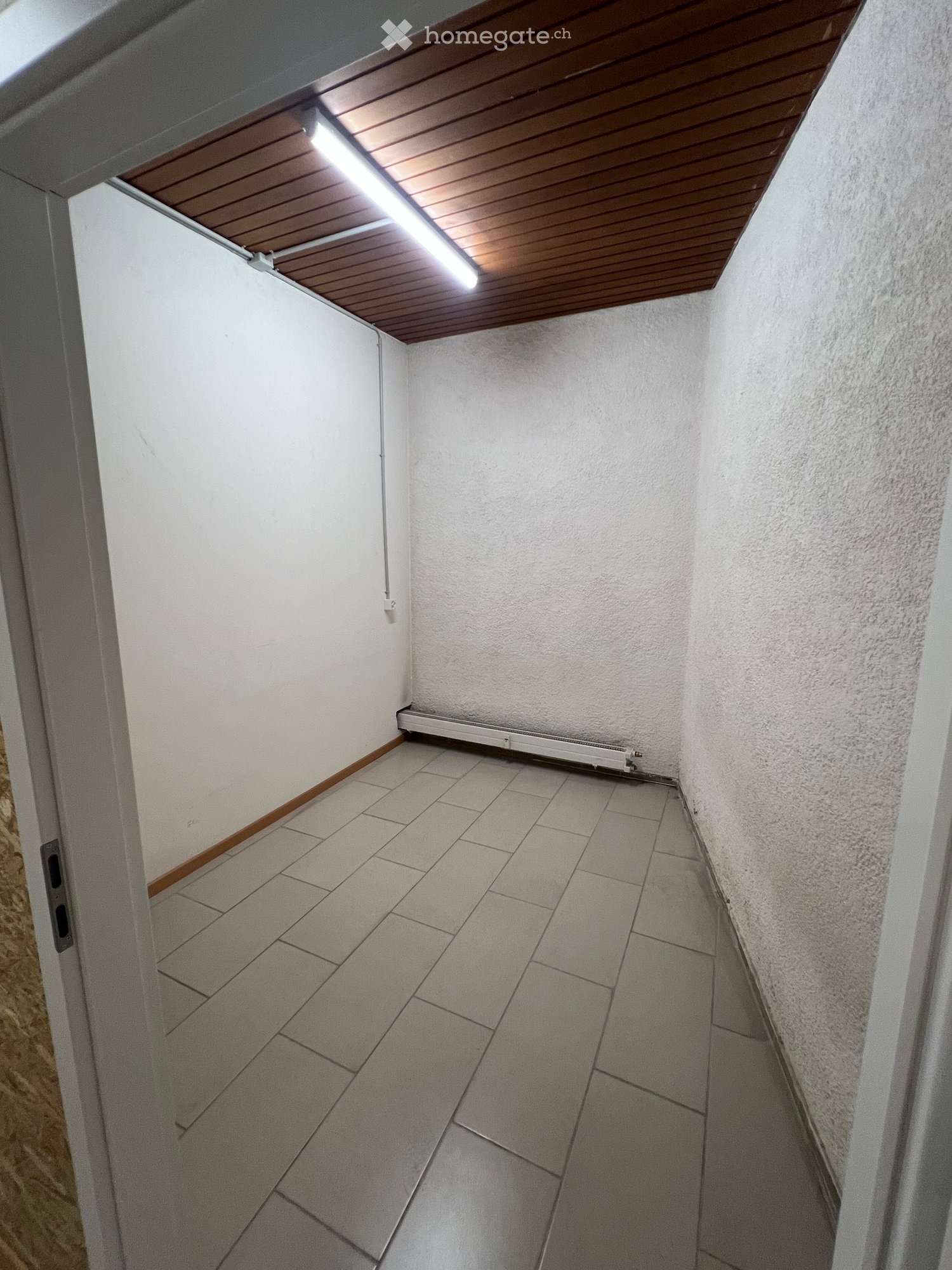 Empty hallway with tiled floor, white walls, wooden trim, and a wooden ceiling with integrated lighting. A radiator is mounted on one wall.