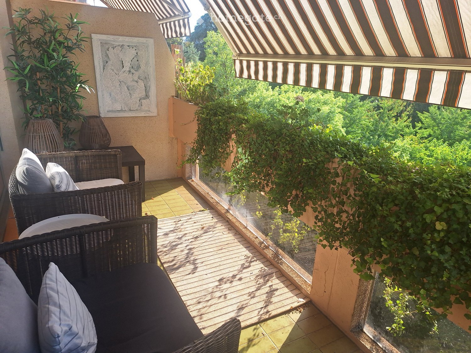 Balcony with wicker sofa, table, vases, and a scenic view of greenery.