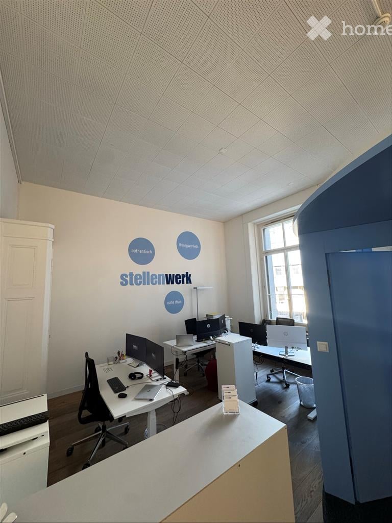 Modern office space with desks, chairs, multiple computer monitors, laptops, keyboards, and a cabinet. The walls are white with blue circular decals and the name "stellenwerk" prominently displayed.