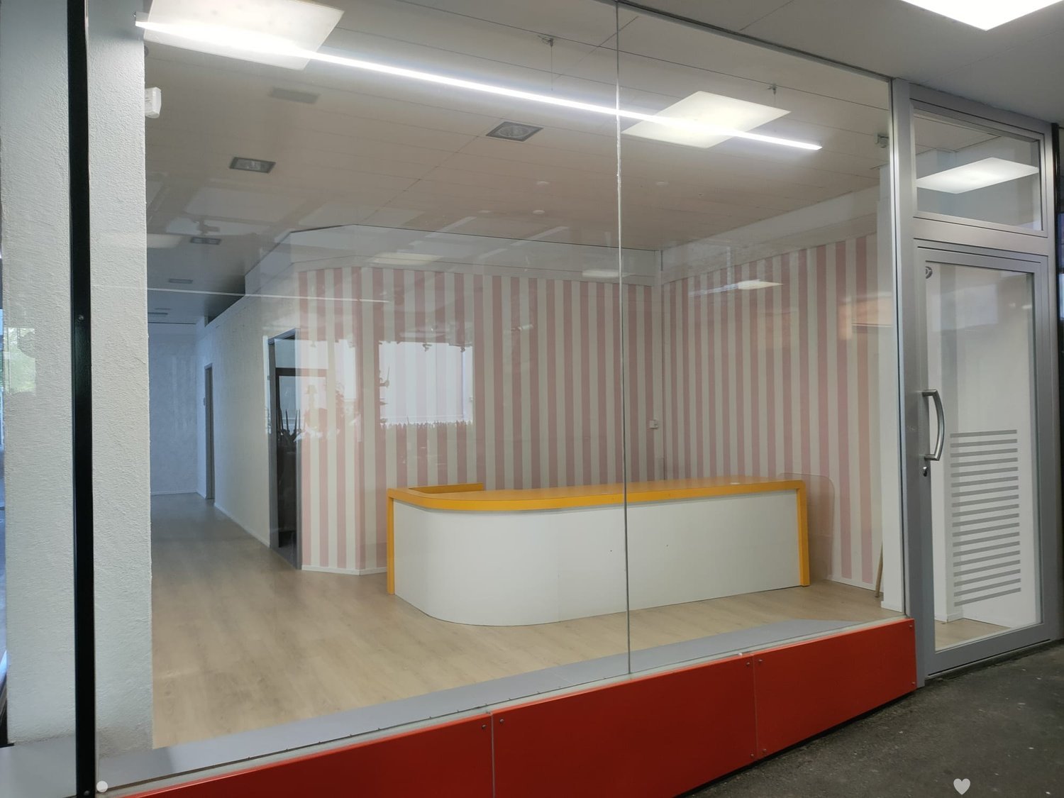 Modern office space with a reception desk, glass partitions, and striped wallpaper in the background.