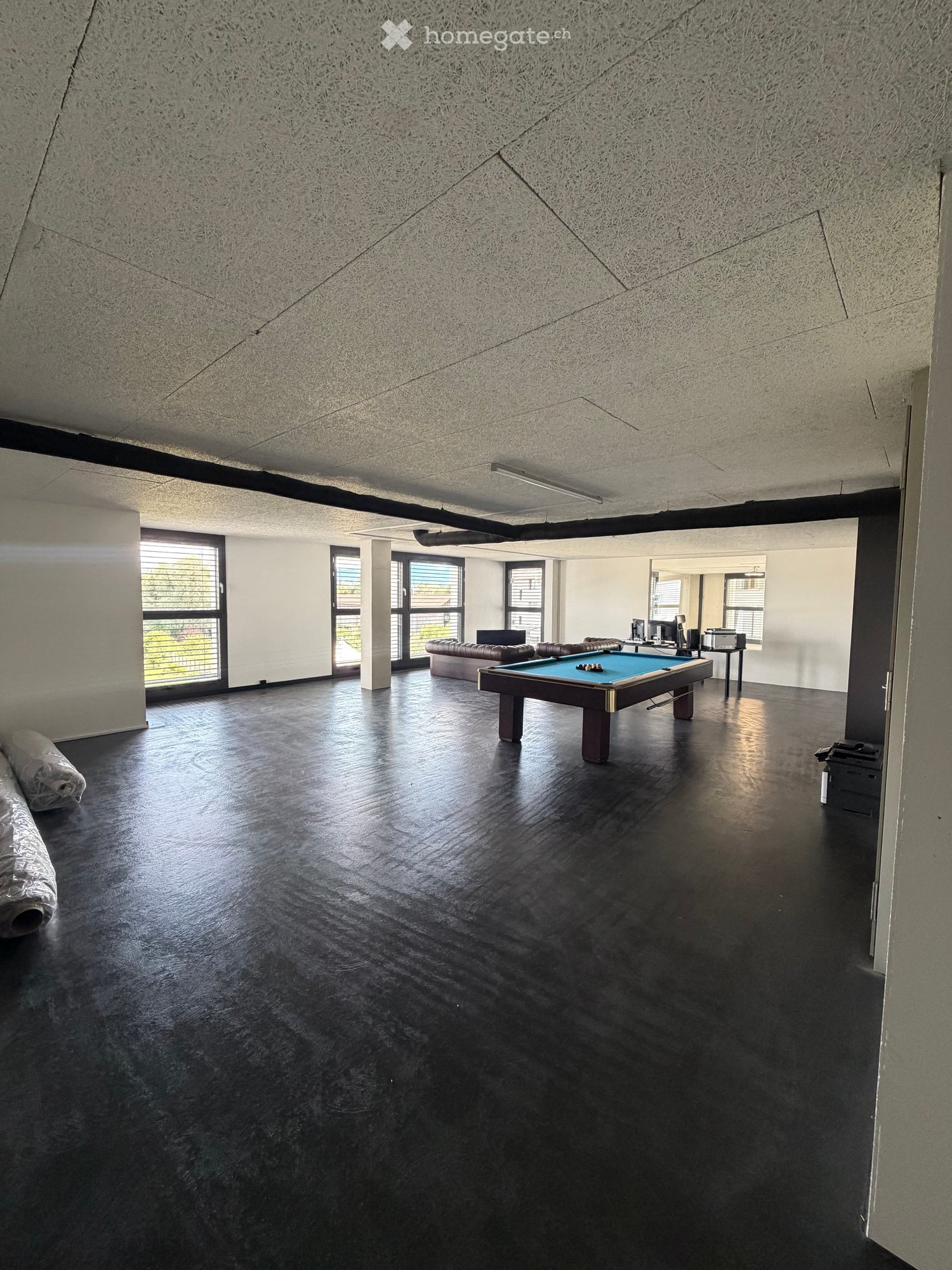 Modern room with dark polished floor, large windows, sofa, pool table, and computer setup.