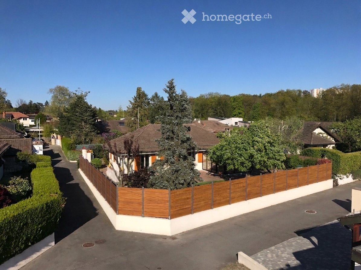 A two-story house with a brown tiled roof, surrounded by a wooden fence and trees, located in a residential neighborhood.