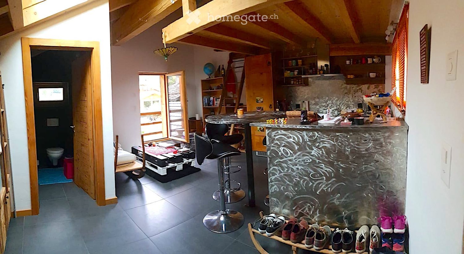 {"visible_features": [], "type": "Living area", "description": "open living area with high wooden ceiling, table, chairs, stools, counter, kitchen and storage shelves, globe, ladder"}