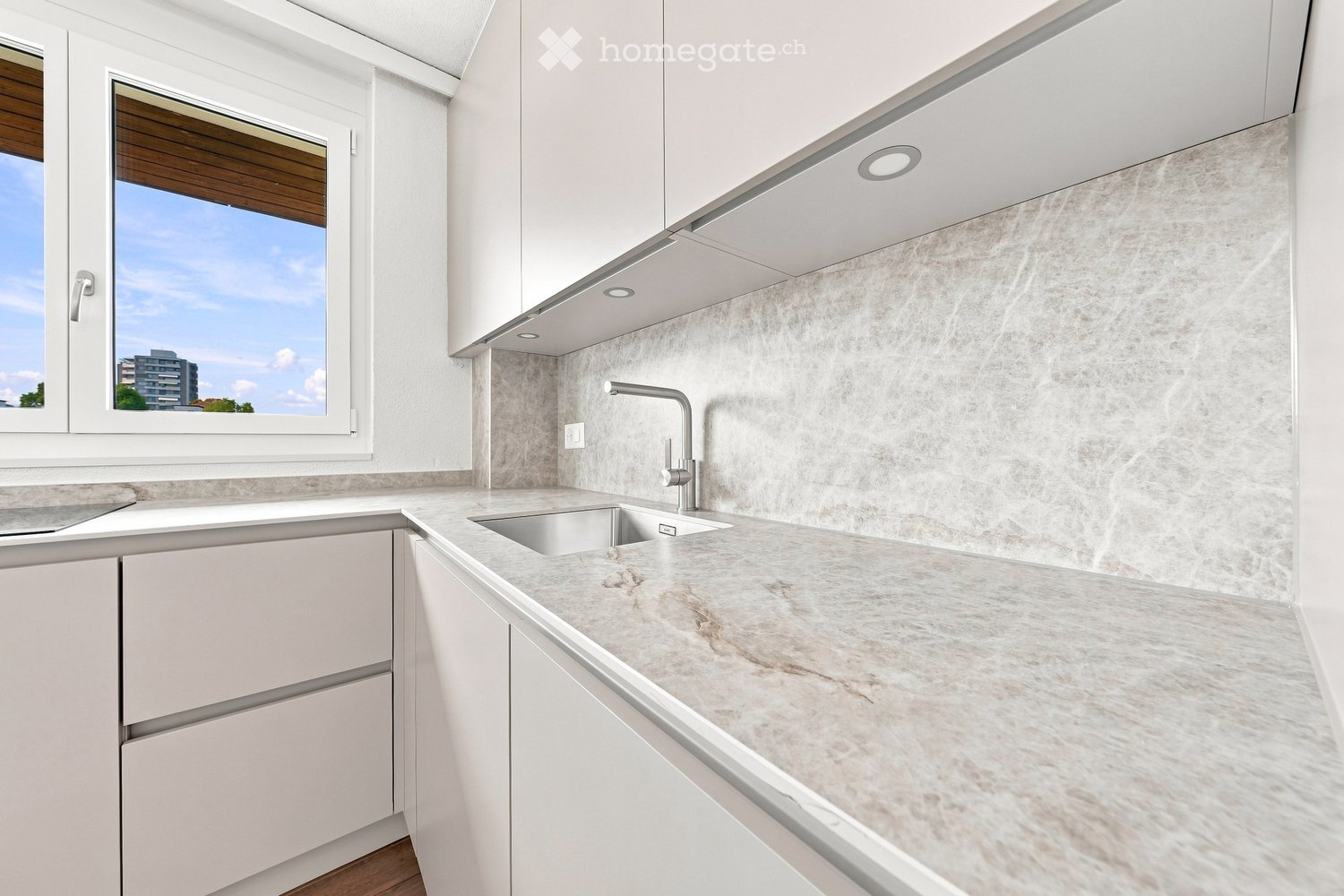 Modern kitchen with white cabinets, marble countertop, and a stainless steel sink with a modern faucet. The backsplash features a textured, light-colored tile design.
