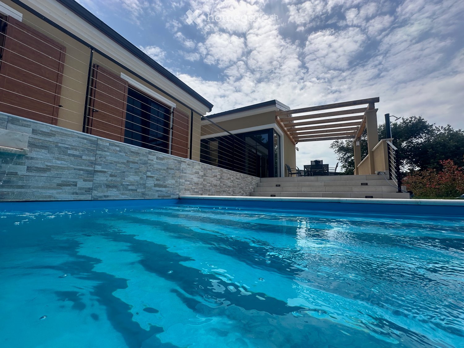 Modern outdoor area with a swimming pool, stone steps leading up to a patio with a pergola and outdoor furniture.