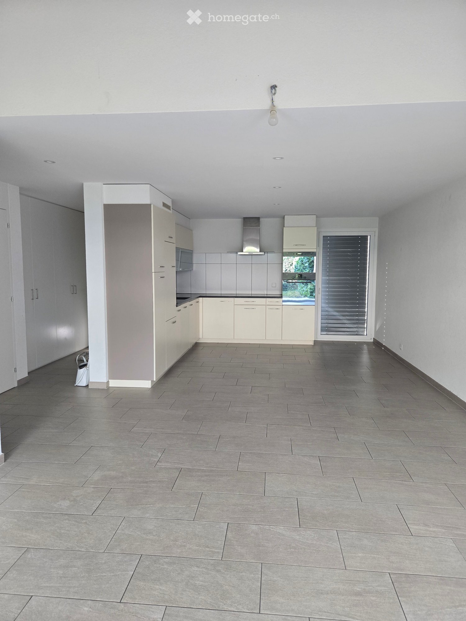 Empty kitchen with light grey tiled floor, white cabinets, and stainless steel appliances. No furniture or items present.