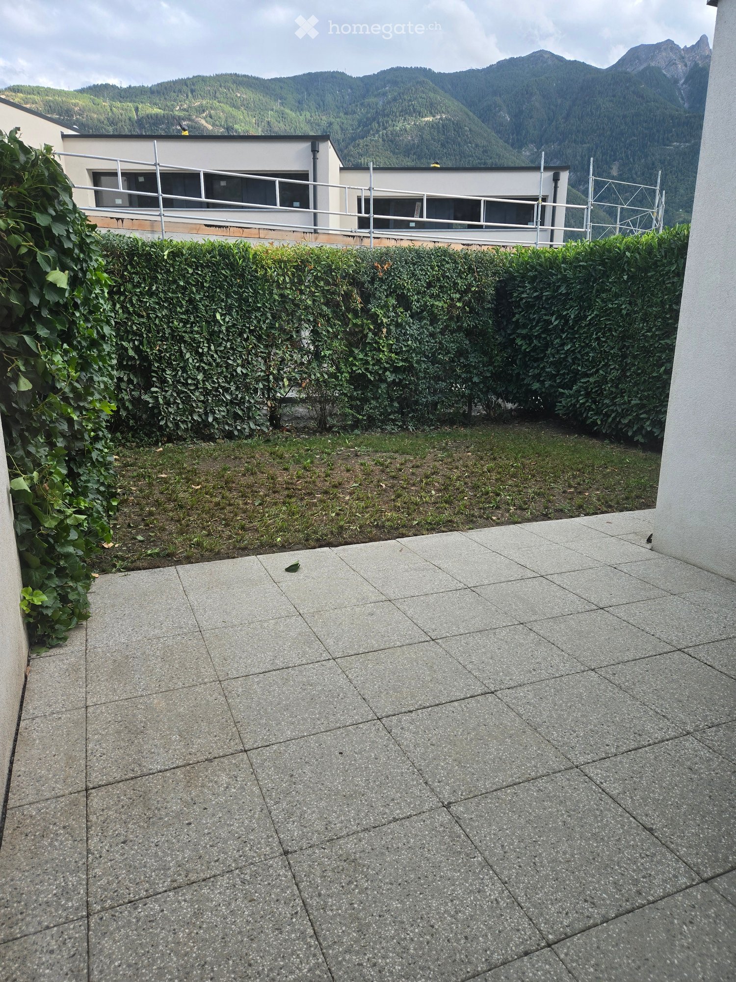 Balcony with tiled floor, metal railing, and a view of a modern building and distant mountains.