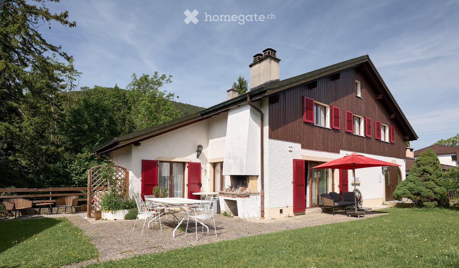 Two-story house with red shutters, white walls, and a wooden facade. Features include a patio with outdoor furniture, a fireplace, and a garden area.