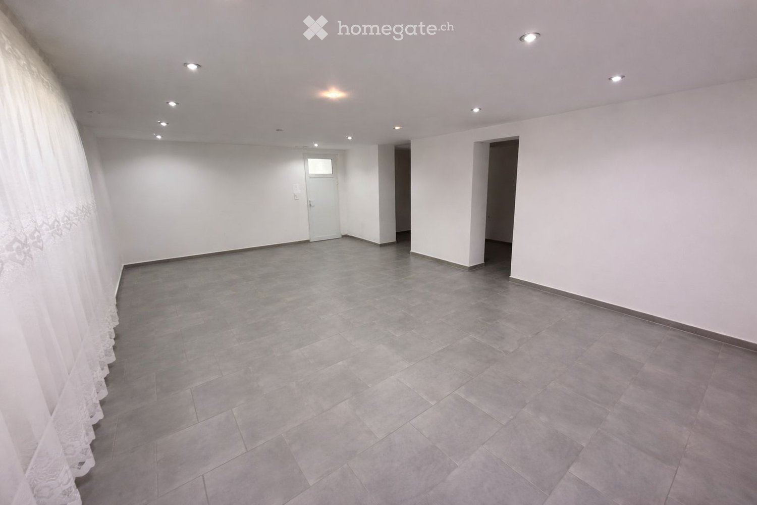 Empty room with white walls, gray tiled floor, a window, and ceiling lights.